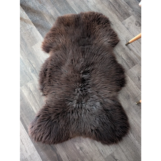 A plush extra large british sheepskin rug in dark brown with natural fluffy texture and irregular edges