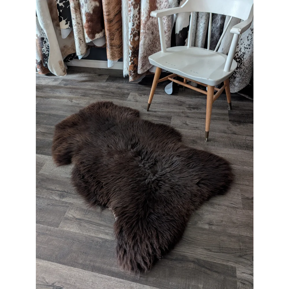 A plush extra large british dark brown sheepskin rug with thick soft fur and natural shape lying on the floor