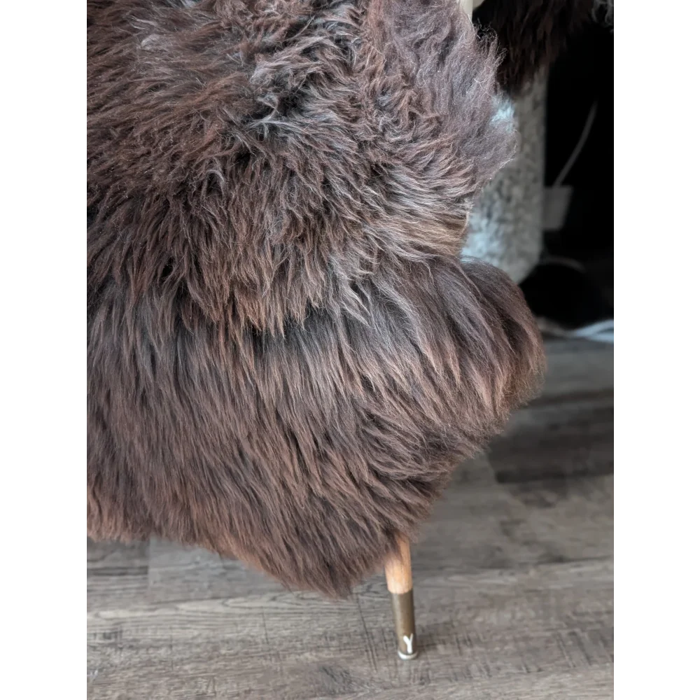 A plush dark brown extra large british sheepskin chair with wooden legs and metallic base for cozy seating