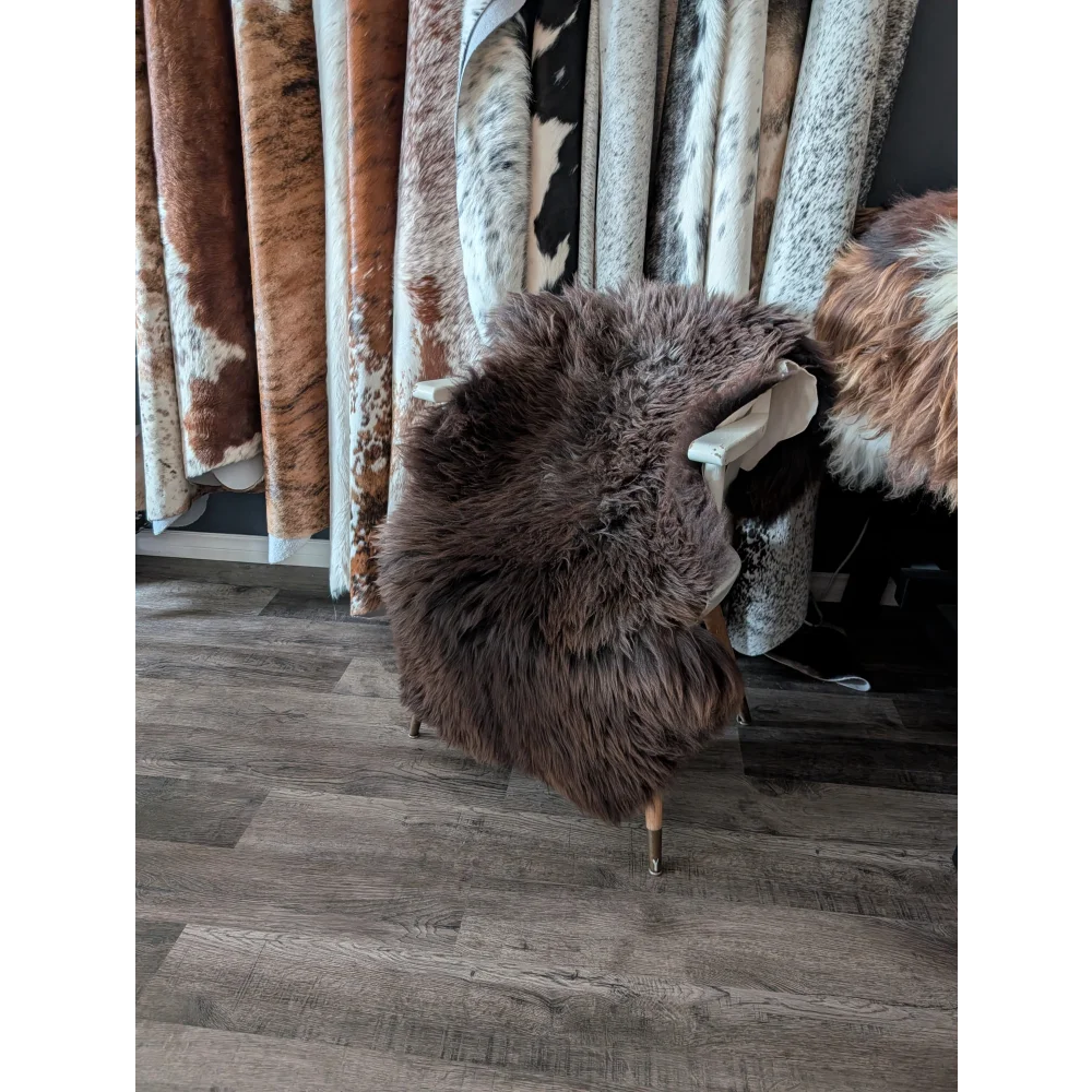 A plush extra large british dark brown sheepskin draped over a chair with slender metal legs