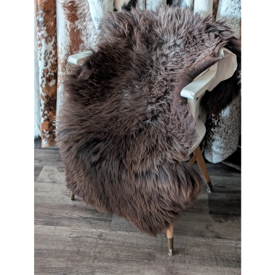 A plush extra large british brown sheepskin rug draped over a white chair showing its long-haired texture