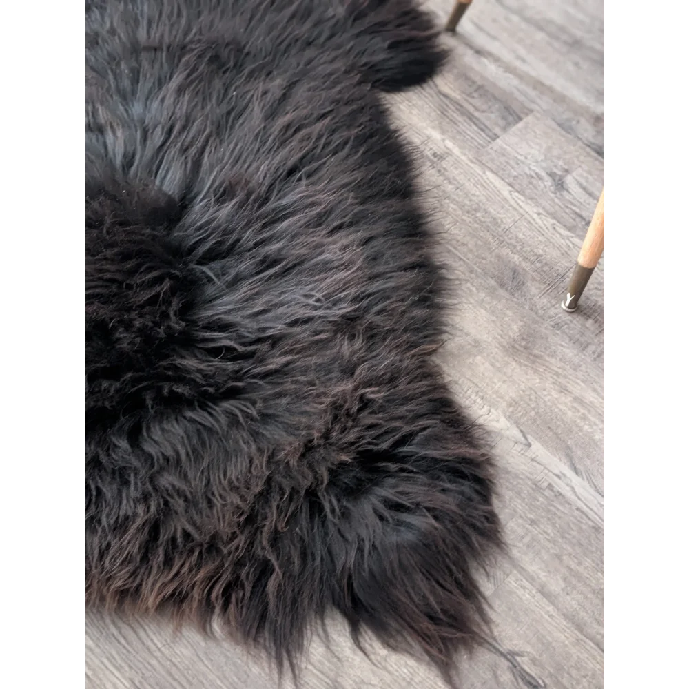 A gorgeous extra large british sheepskin rug in dark charcoal black with long dense fur on gray wood floor by angus oliver canada