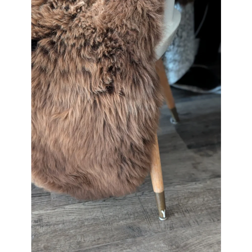 A plush brown sheepskin rug draped over a wooden leg chair with metallic caps from angus oliver canada collection