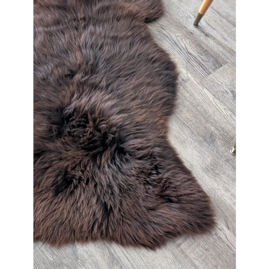 A plush extra large british sheepskin rug in dark brown with soft dense fur and a natural irregular shape