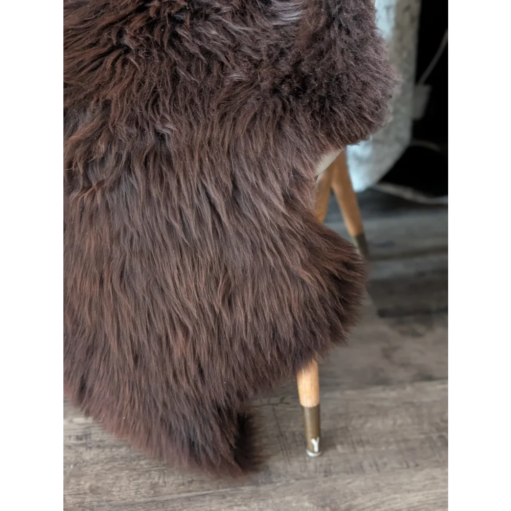 A plush dark brown angus oliver sheepskin rug draped over a modern chair with light wood legs and metallic caps canada