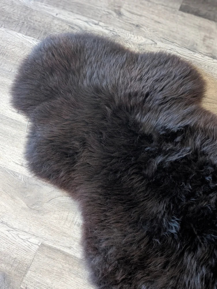 A dark charcoal british isles sheepskin rug with soft fluffy texture and natural irregular edges 53 by 27 inches