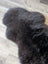 A dark charcoal british isles sheepskin rug with soft fluffy texture and natural irregular edges 53 by 27 inches