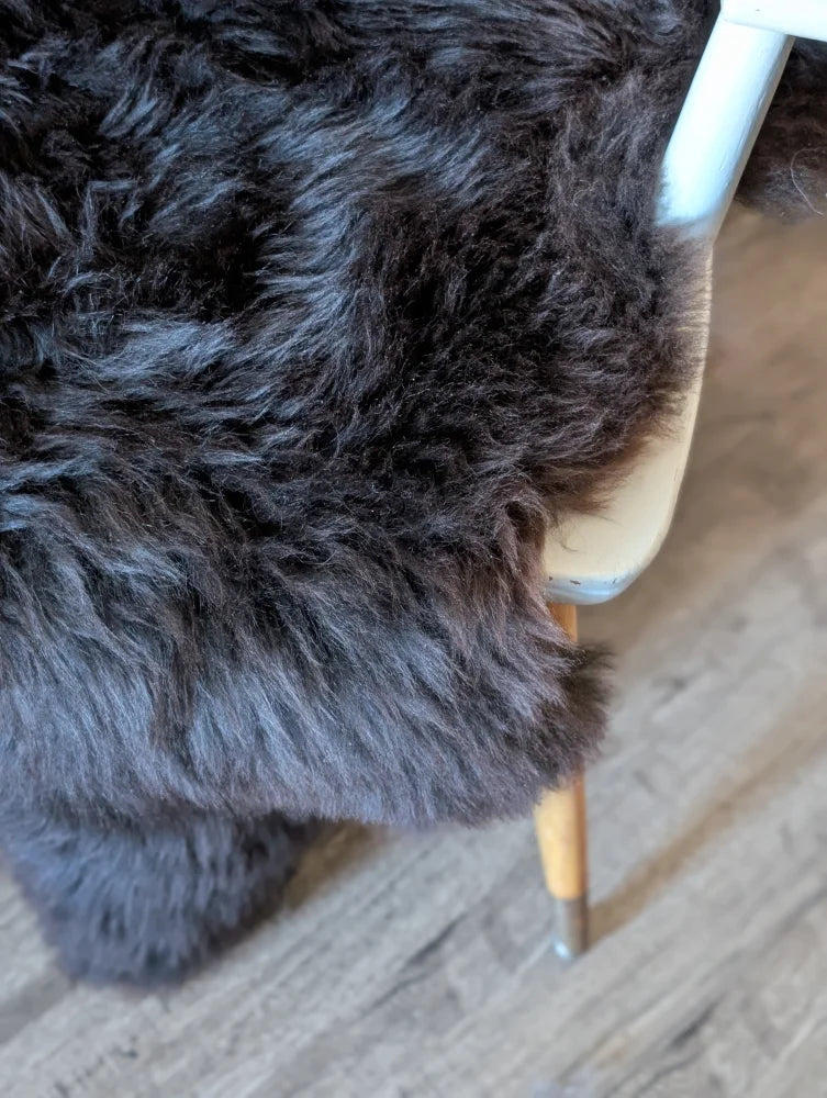A plush dark gray british isles sheepskin rug with thick shaggy faux fur draped over a chair edge
