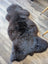 A plush dark gray british isles sheepskin rug with soft dense fur and a natural irregular shape measuring 53 x 27 inches