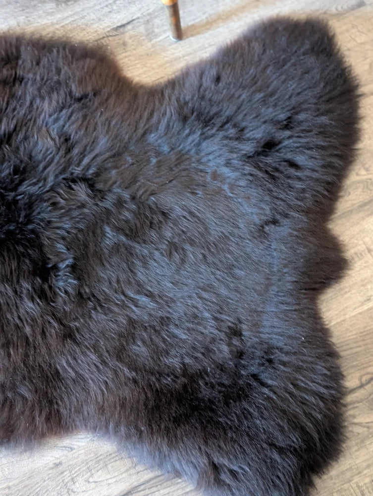 A plush dark gray british isles sheepskin rug with soft dense fur and natural irregular shape measuring 53 by 27 inches