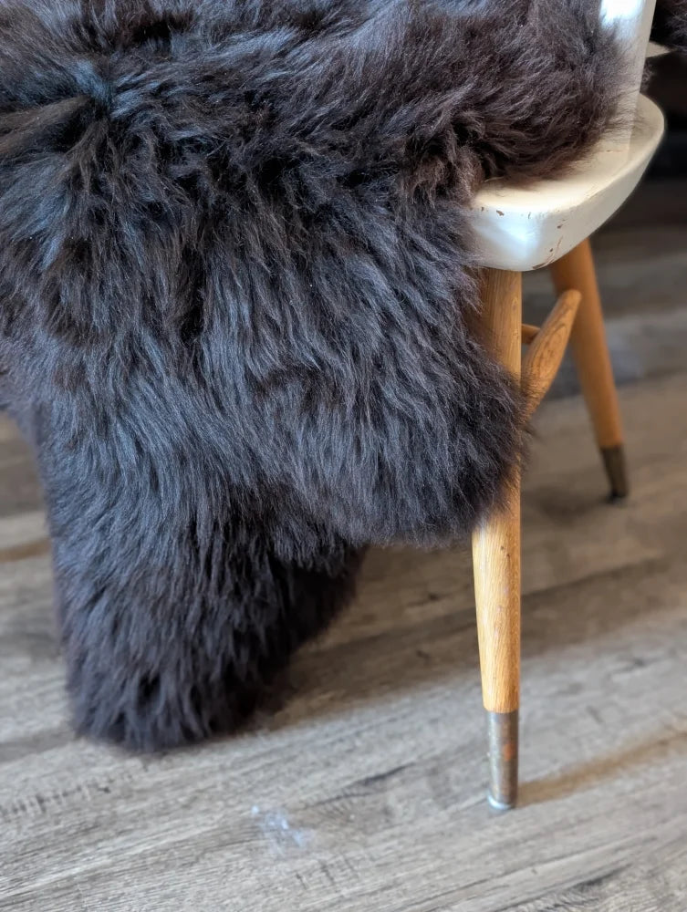 Dark gray plush british isles sheepskin rug draped over white stool with wooden legs for cozy decor