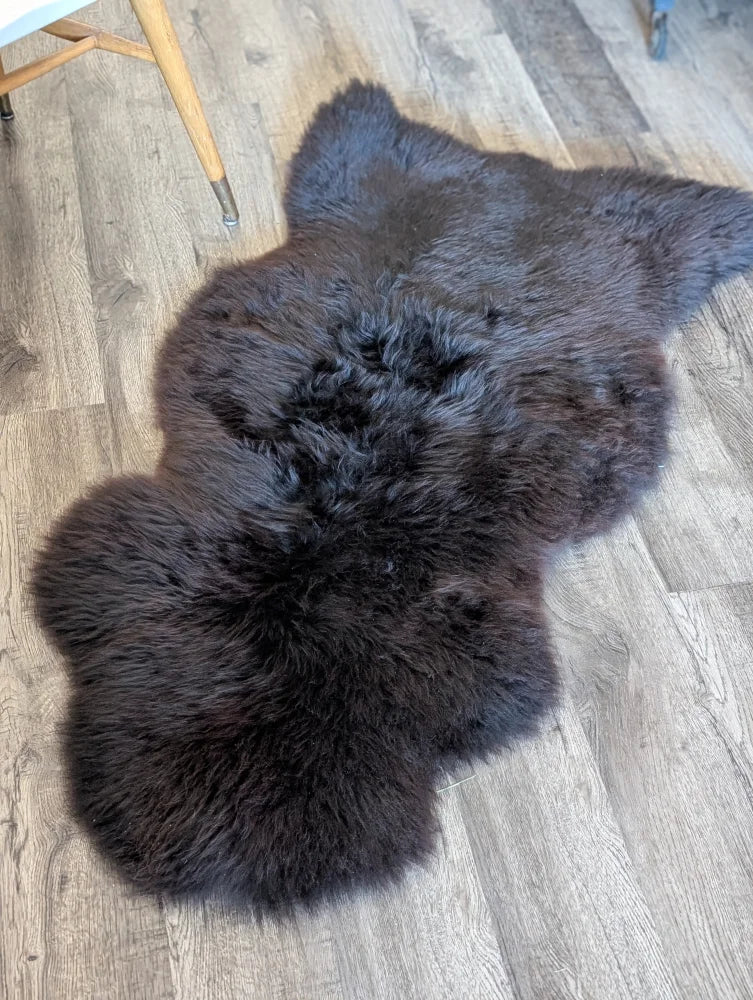 A plush dark brown british isles sheepskin rug with natural shape and soft dense fur measuring 53 by 27 inches