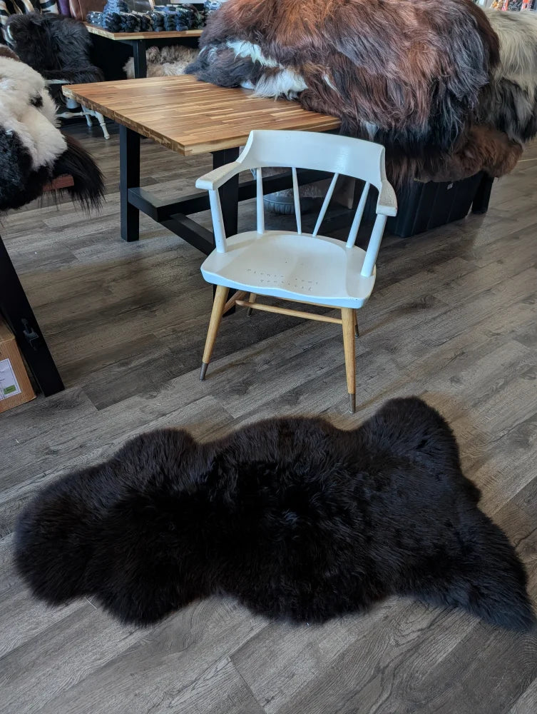 Black british isles sheepskin rug with plush fluffy texture and natural irregular edges measuring 53 x 27 inches