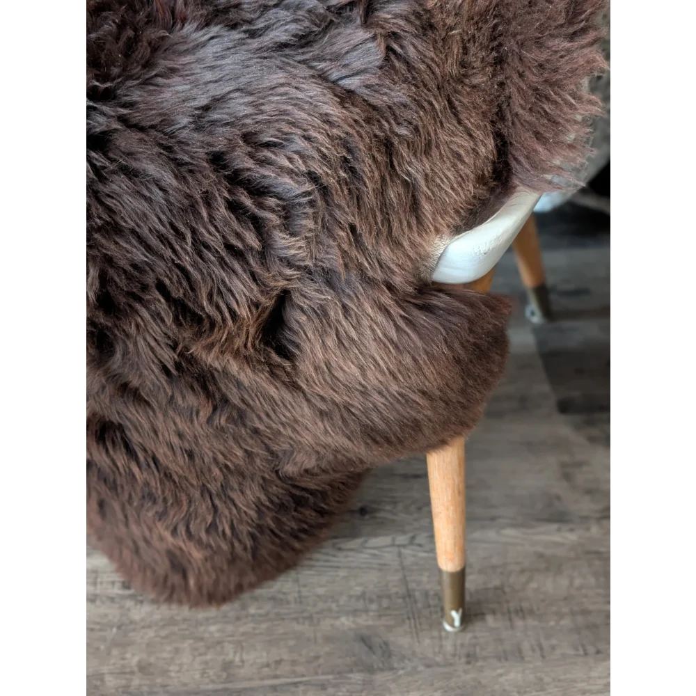 A plush dark brown british sheepskin rug draped over a modern chair back with wooden legs by angus oliver
