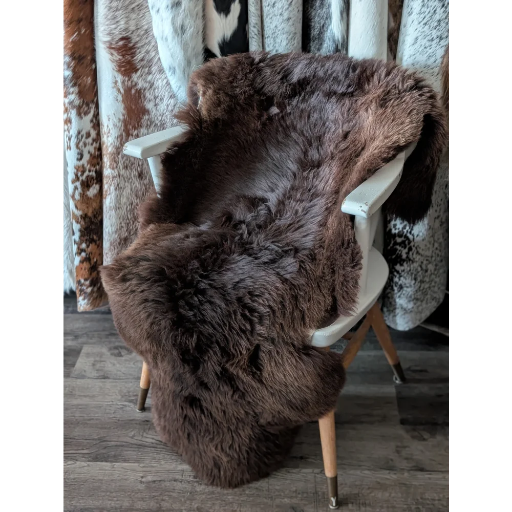 A gorgeous extra large dark brown british sheepskin rug draped over a white wooden chair by angus oliver