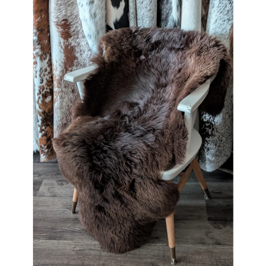 A gorgeous extra large dark brown british sheepskin rug draped over a white wooden chair by angus oliver