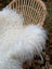A plush off-white long wool icelandic sheepskin throw with curly fibers draped over a woven wicker chair