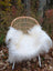 White fluffy curly long wool icelandic sheepskin throw draped over woven rattan chair with white metal legs