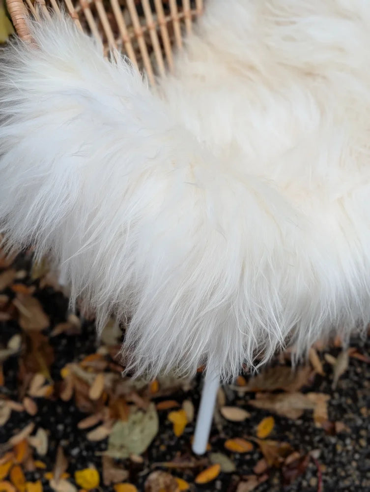 White fluffy wool icelandic sheepskin throw blanket draped over a wicker chair for cozy decor