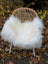 A cozy white long wool icelandic sheepskin throw draped over a woven wicker chair with metal legs