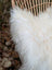 A plush off-white wool icelandic sheepskin throw with long soft fibers draped over a woven wicker chair