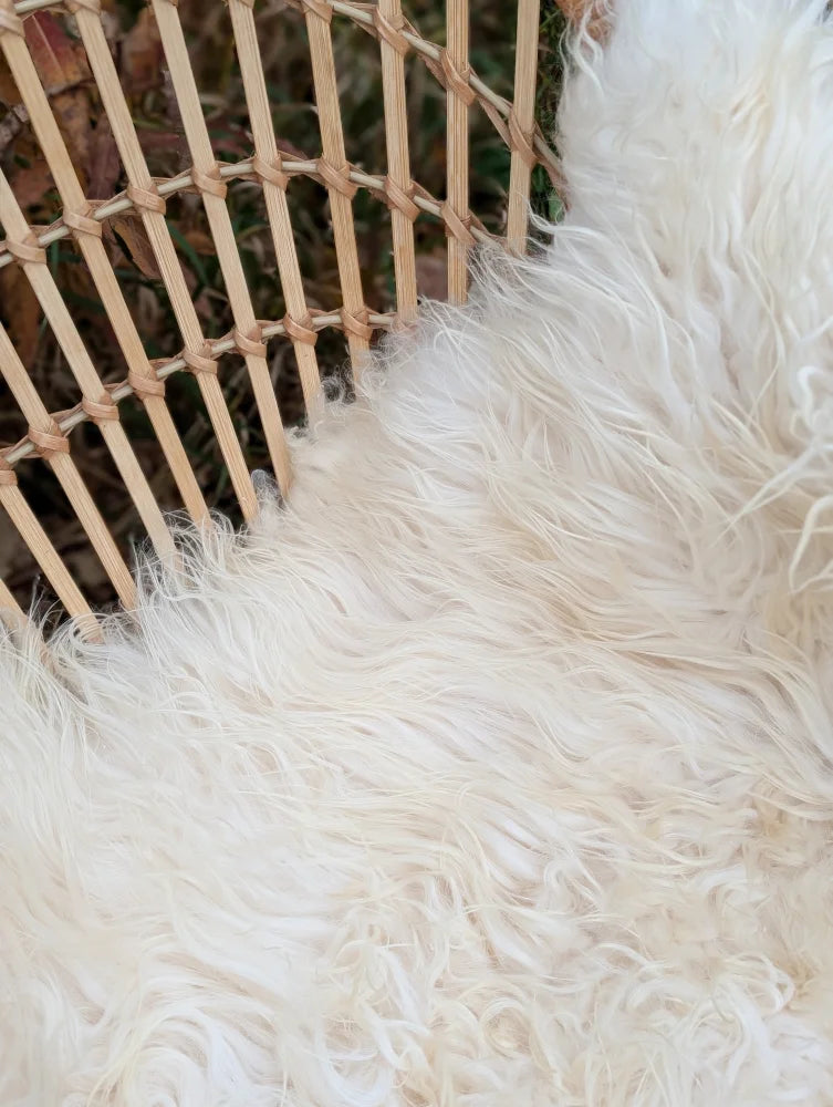 A plush off-white ice#4 48 x 27 inch curly long wool icelandic sheepskin rug next to a wicker chair