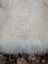 A plush off-white long wool icelandic sheepskin rug with curly fibers measuring 48 by 27 inches