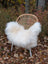 A cozy white curly long wool icelandic sheepskin throw draped over a woven rattan chair with metal legs
