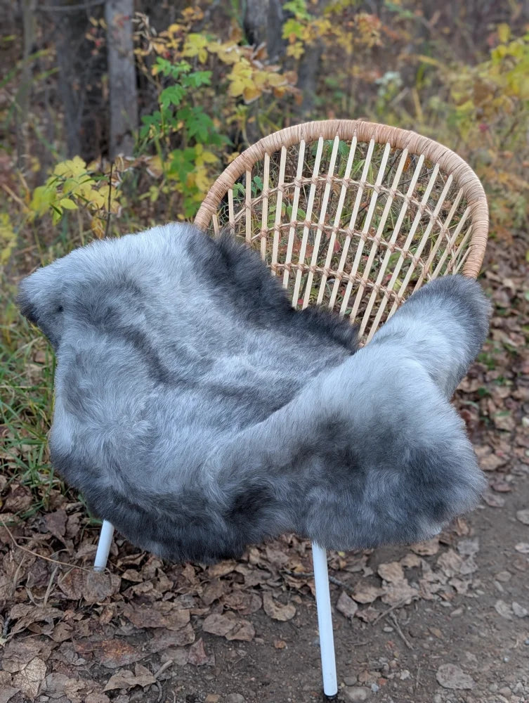 Gray faux fur throw draped over a wicker chair featuring long wool icelandic sheepskin in natural grey color