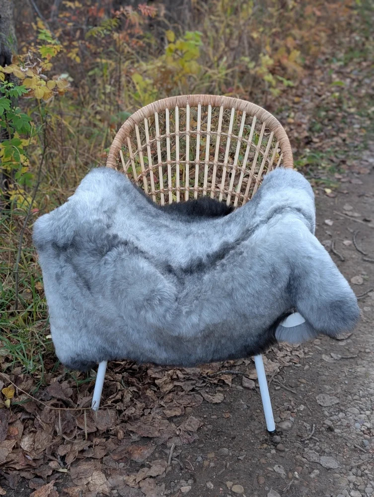 Gray faux fur throw draped over wicker chair with white metal legs made of long wool icelandic sheepskin