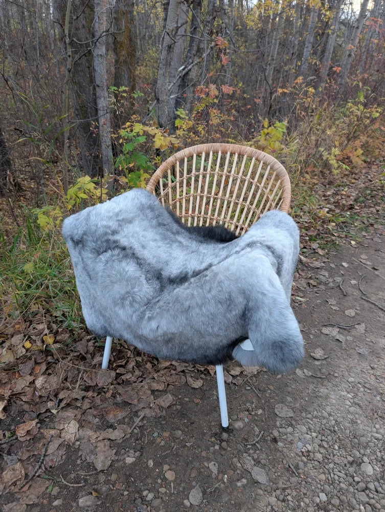 Gray faux fur throw with wool icelandic texture draped over a wicker chair with white metal legs