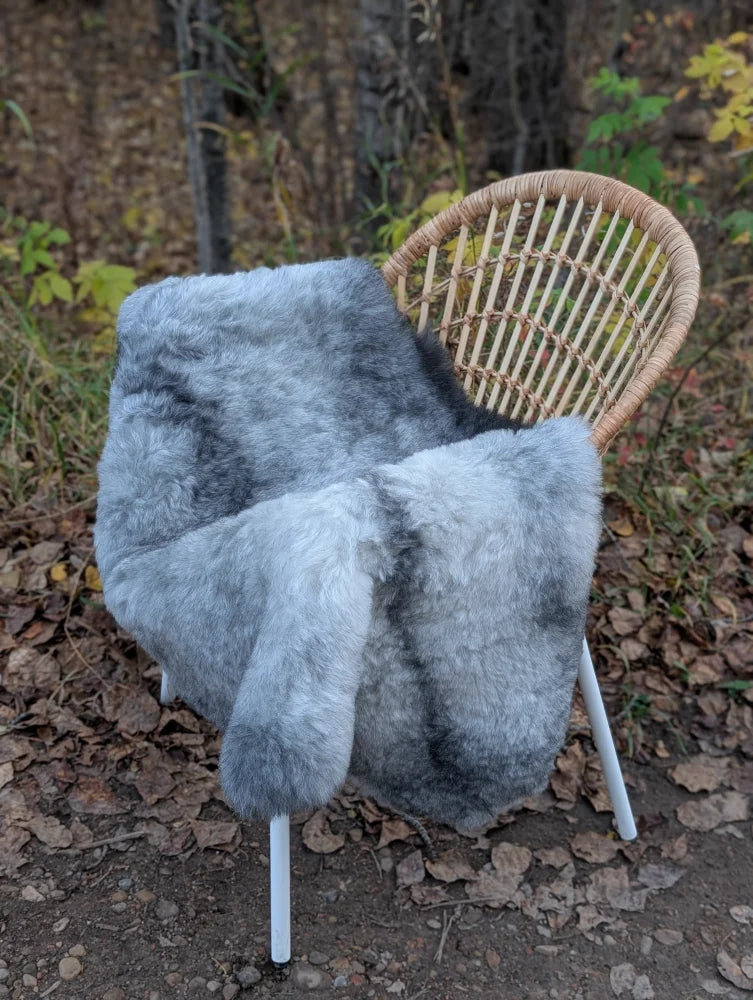 Gray faux fur throw blanket draped over wicker chair made from long wool icelandic sheepskin in natural grey