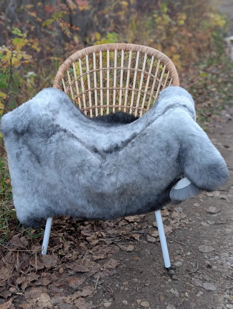 Gray faux fur throw draped on wicker chair featuring massive 53x32 long wool icelandic sheepskin natural grey design