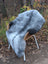 A plush natural grey icelandic sheepskin rug with long wool draped over a wicker chair with white metal legs