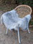 A soft gray long wool icelandic sheepskin throw draped over a wicker chair with white metal legs