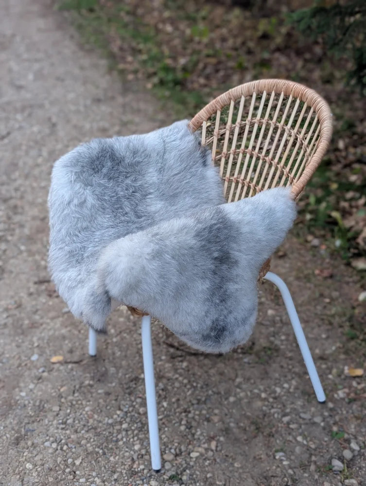 A soft light gray long wool icelandic sheepskin throw draped over a wicker chair with white metal legs