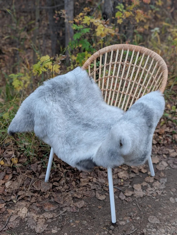 Gray faux fur throw draped over wicker chair with white metal legs featuring long wool Icelandic sheepskin texture