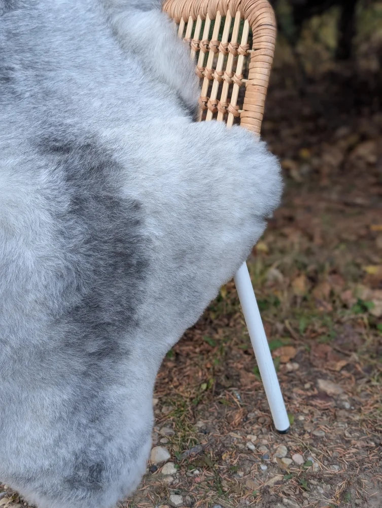 A soft gray wool icelandic sheepskin throw draped over a wicker chair perfect for cozy decor