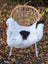 A cozy white and black cow print icelandic sheepskin chair cover made of short wool draped over a wicker chair with metal legs