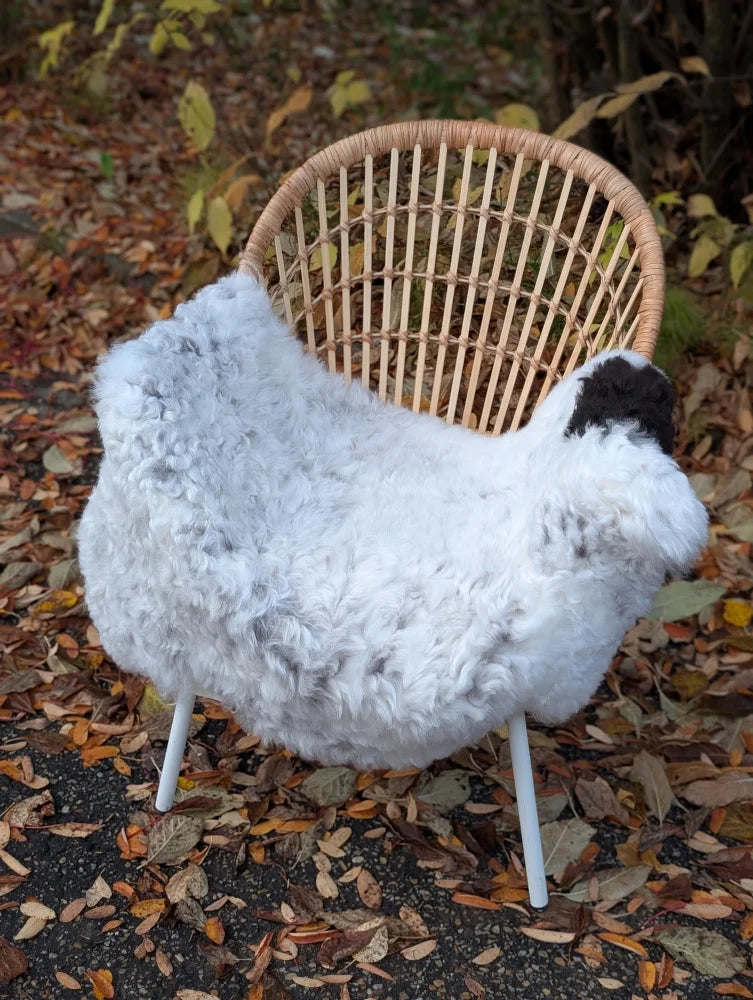 White sheep shaped chair cover with black face made of fluffy faux fur on medium spotted icelandic sheepskin rug