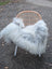 A cozy wool icelandic sheepskin in natural grey draped over a wicker chair with slender white legs