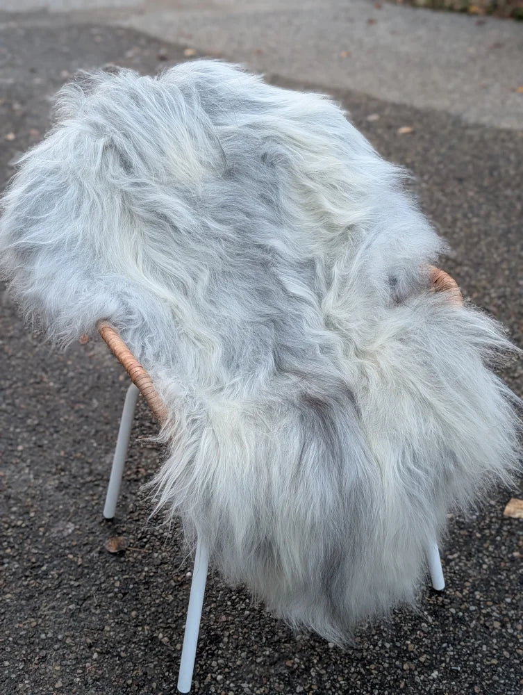 A fluffy grey icelandic sheepskin rug draped over a chair with woven wooden armrests showing long wool icelandic texture