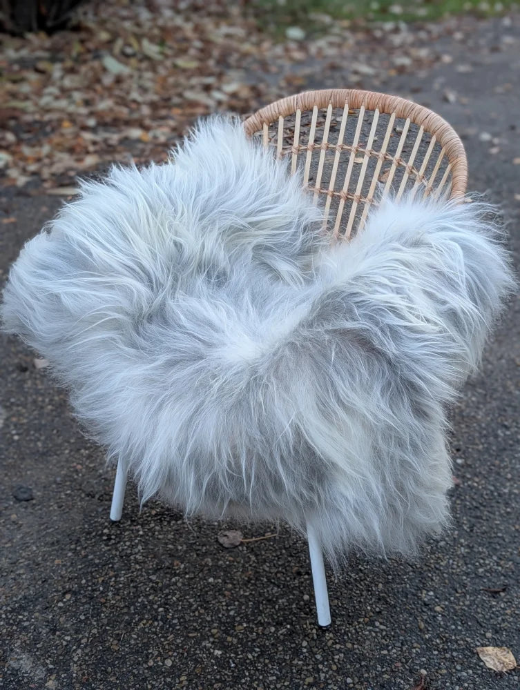 A plush grey icelandic sheepskin throw with long wool draped over a wicker chair with white metal legs