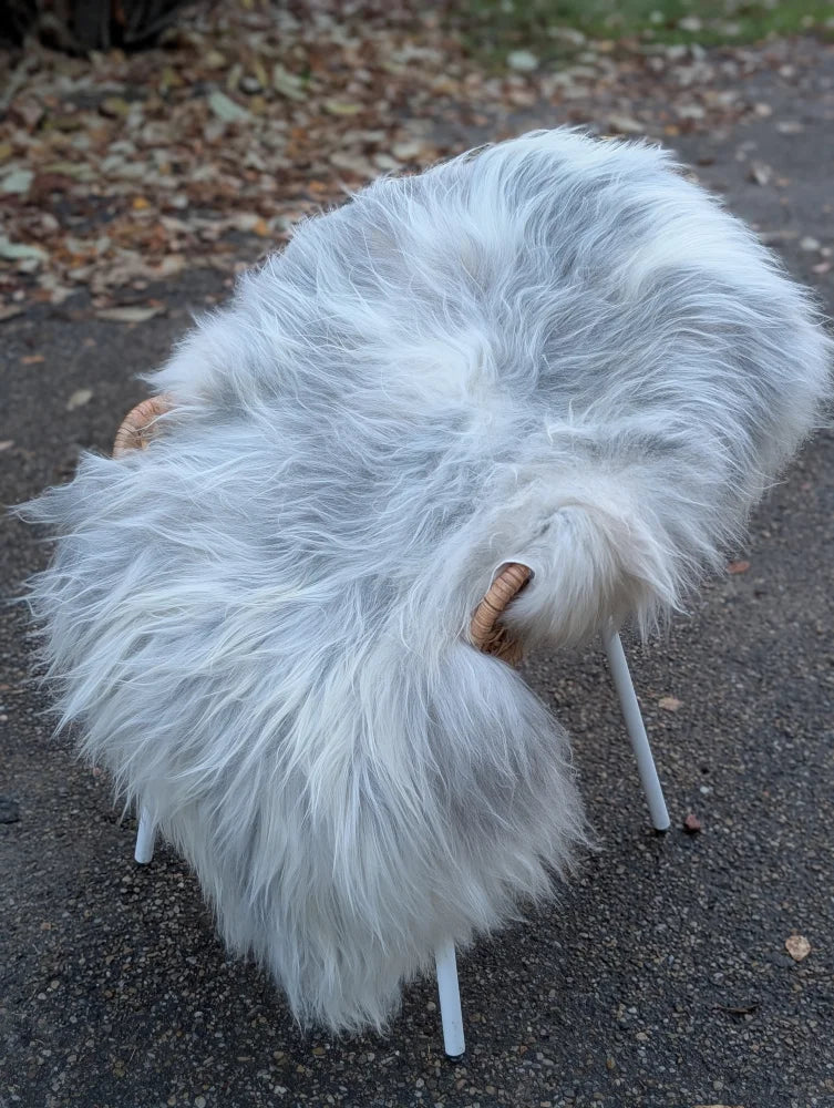 A plush white sheep-shaped chair with wooden horns and slender legs made from long wool Icelandic sheepskins
