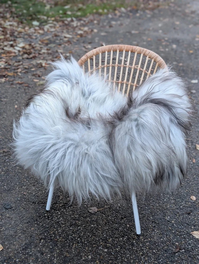 A long wool icelandic fluffy grey icelandic sheepskin throw draped over a woven wicker chair with metal legs