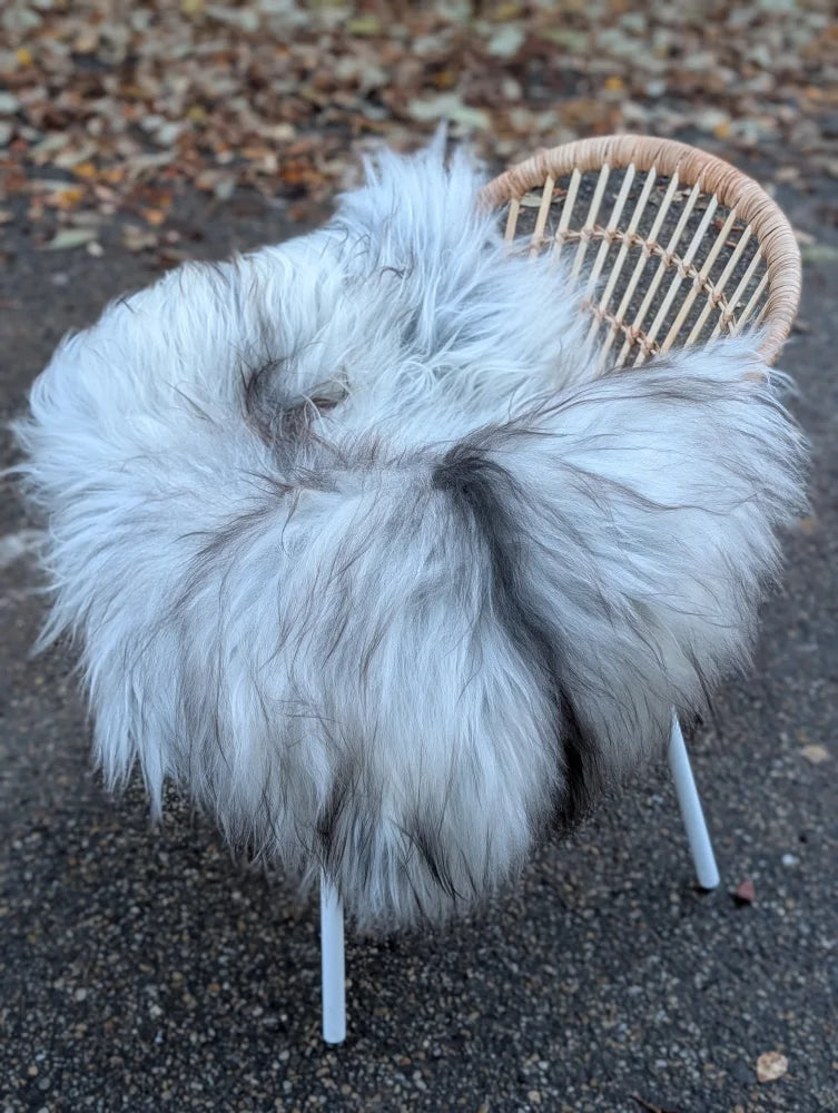 A plush grey icelandic sheepskin wool throw draped over a wicker chair with slender metal legs