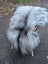 A plush long wool icelandic sheepskin rug in natural grey draped over a wicker chair with white legs