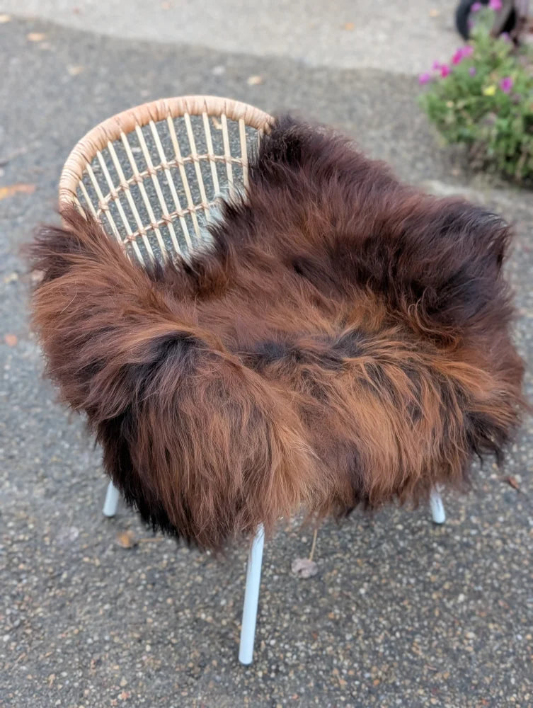 A cozy thick dark rusty icelandic sheepskin rug draped over a wicker chair with white metal legs
