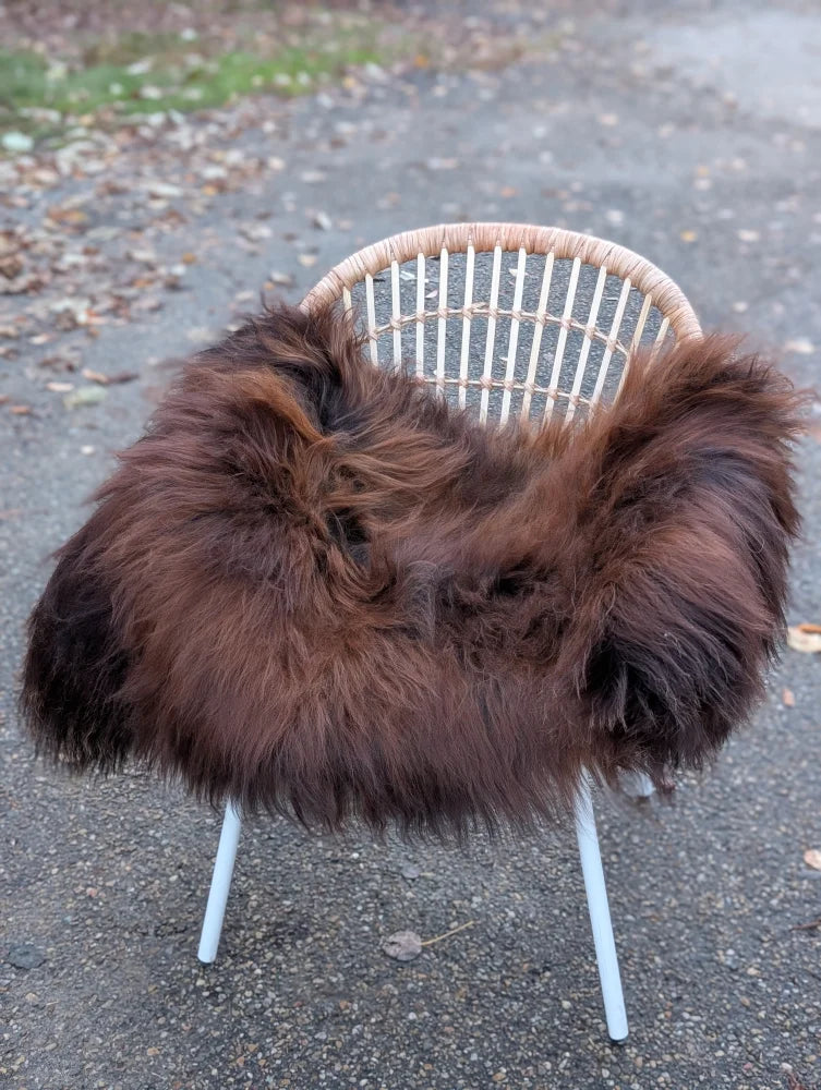 A plush long wool icelandic sheepskin rug in dark rusty draped over a white wicker chair for cozy decor