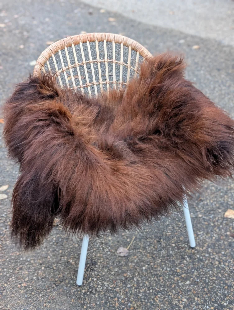 A plush long wool icelandic sheepskin rug in dark rusty color draped over a wicker chair for cozy decor